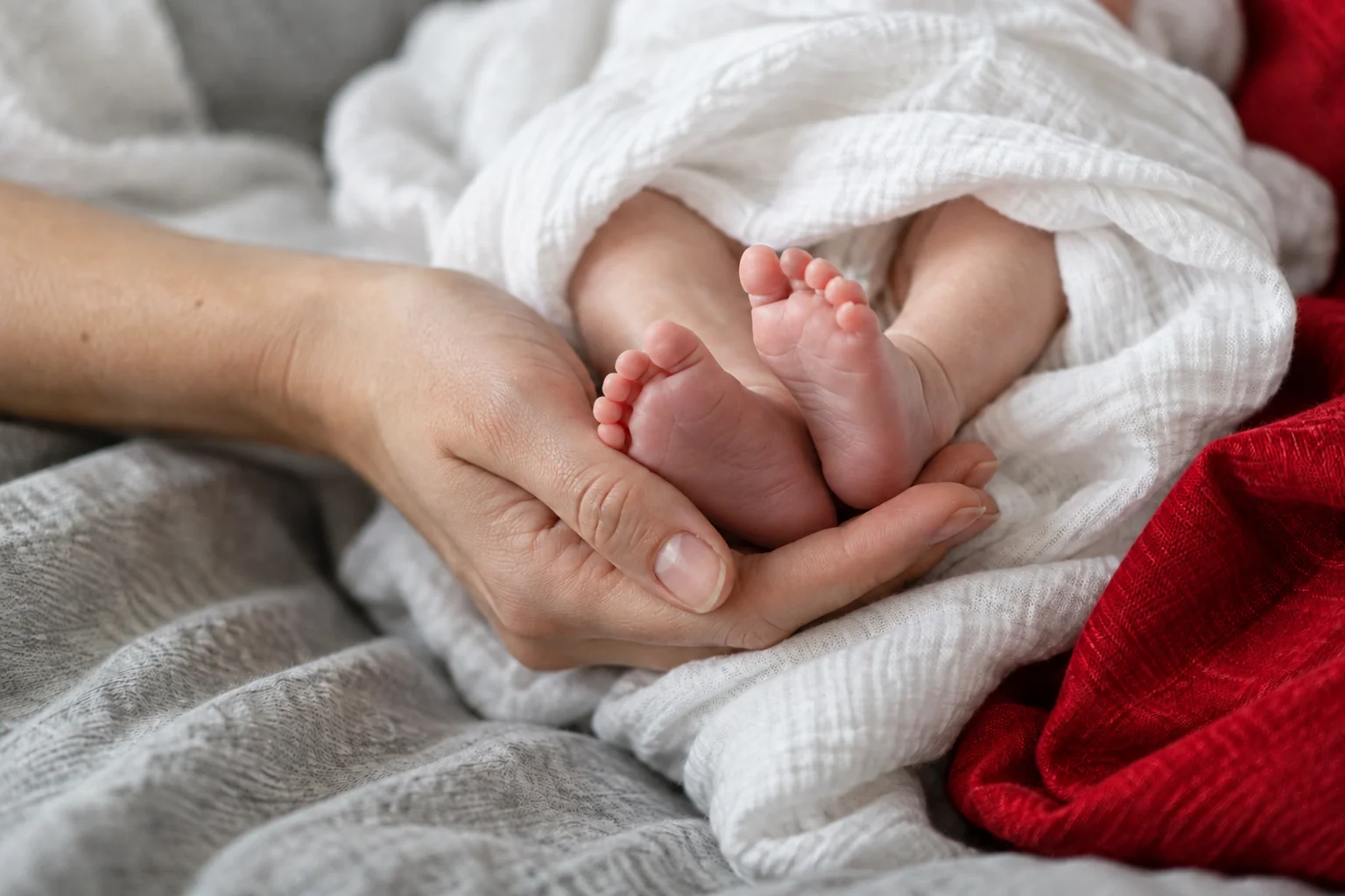 Kleine Babyfüße in den Händen eines Erwachsenen, mit roter Decke und ohne erkennbare Gesichter